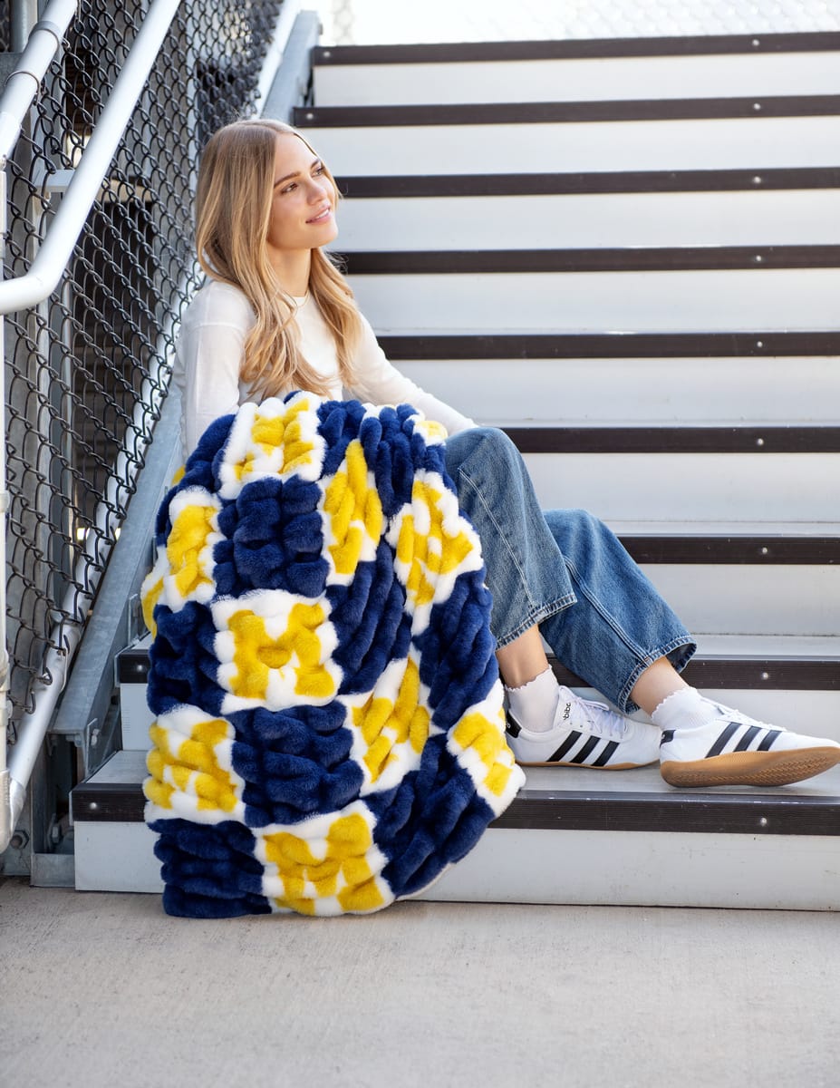 University of Michigan Wolverines Blanket draped on a young woman sitting on stairs, showcasing the vibrant blue and yellow pattern.