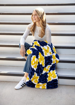 University of Michigan Wolverines Blanket draped over a woman sitting on stairs, showcasing its soft colors and design.