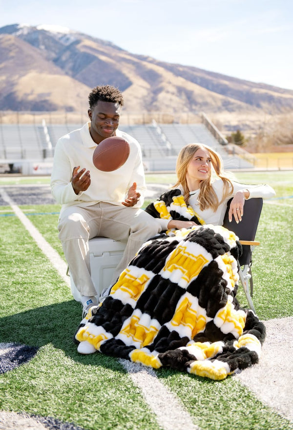 Hugs University of Idaho Vandals Blanket draped over a woman sitting with a man on a football field.