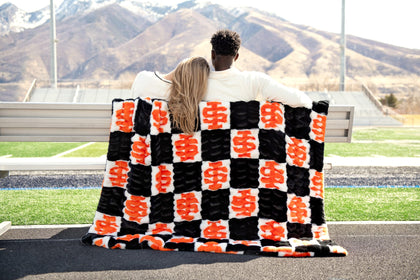 Hugs Idaho State Bengals Blanket used by a couple on a bench showcasing school spirit in bold black and orange.