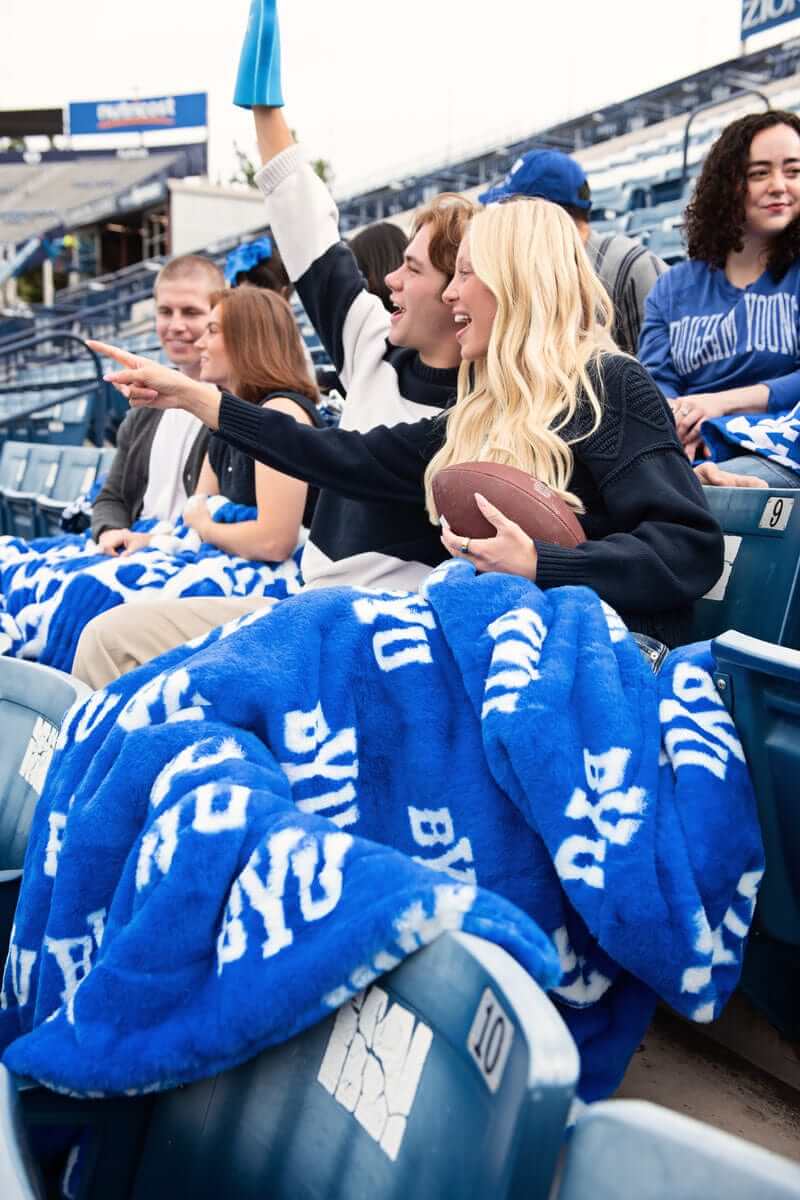 Minky Couture BYU Cougars Blanket featured in a vibrant blue color with fans cheering at a game.