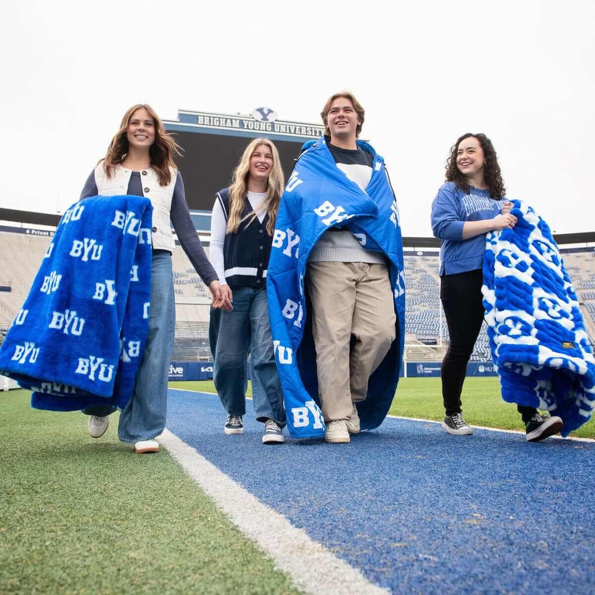 Group of friends walking in BYU Cougars Blanket on the football field, showing school spirit.