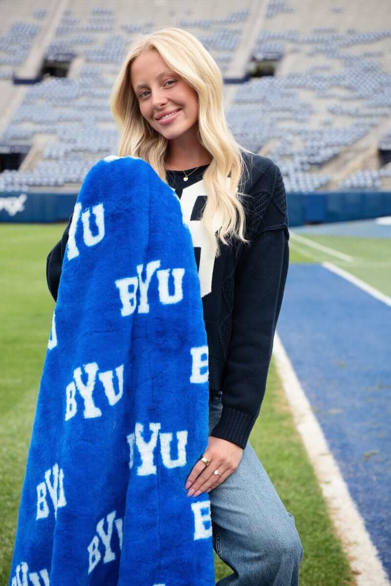 Young woman on the field holding a Minky Couture BYU Cougars Blanket showcasing its vibrant blue and white design.