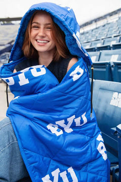 Woman wearing the Minky Couture BYU Cougars Hooded Stadium Blanket in a stadium setting, showcasing team spirit.