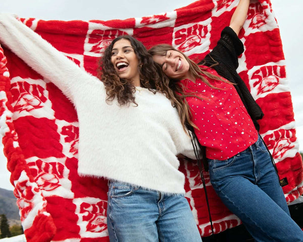 Two friends celebrating under a red and white Southern Utah Thunderbirds blanket.