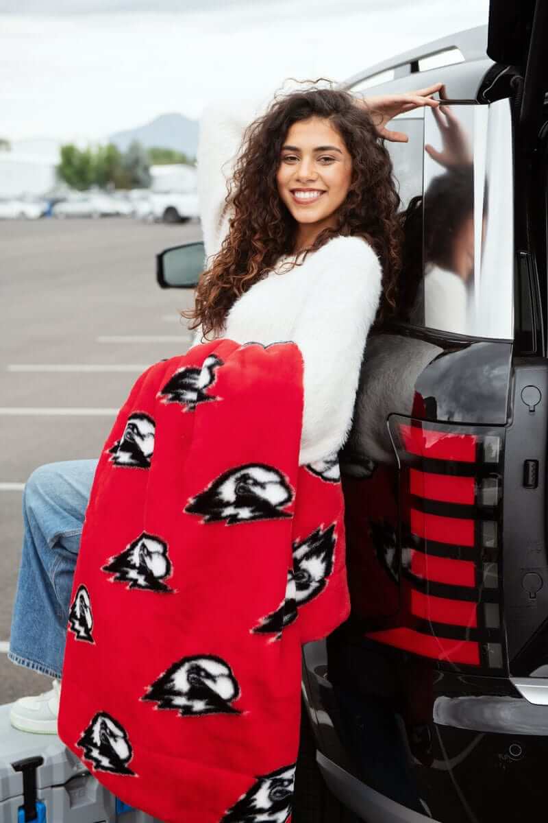 Woman sitting in truck bed wrapped in Southern Utah Thunderbirds red blanket.