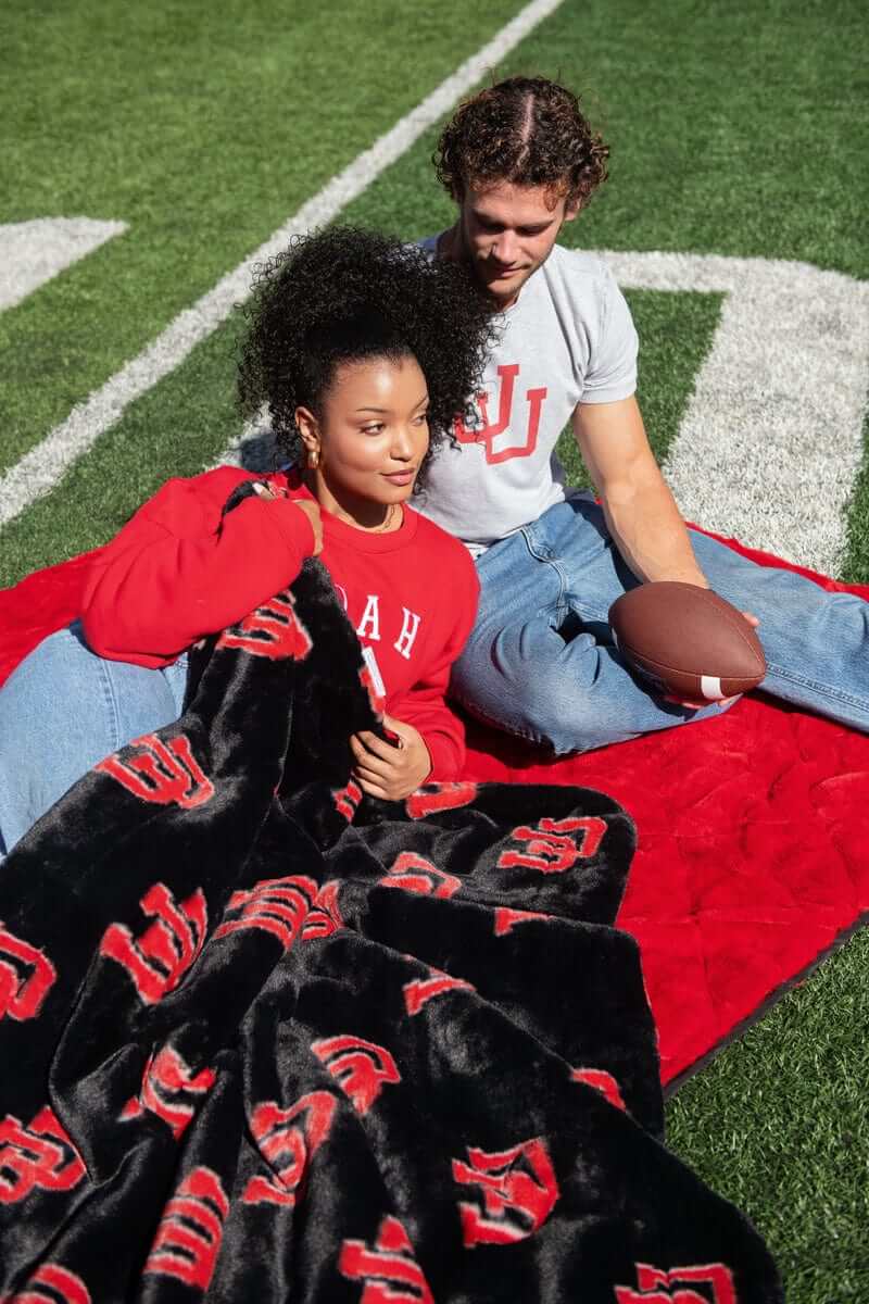 Couple sitting on field with black and red U logo University of Utah Minky Couture plush blanket.