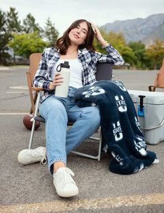 Woman relaxing in tailgate chair with navy Utah State Aggies blanket and water bottle.