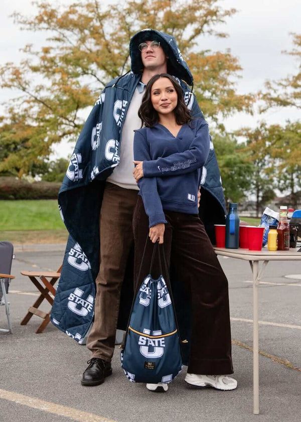 Couple wearing Minky Couture navy Utah State Aggies blankets at tailgate party.