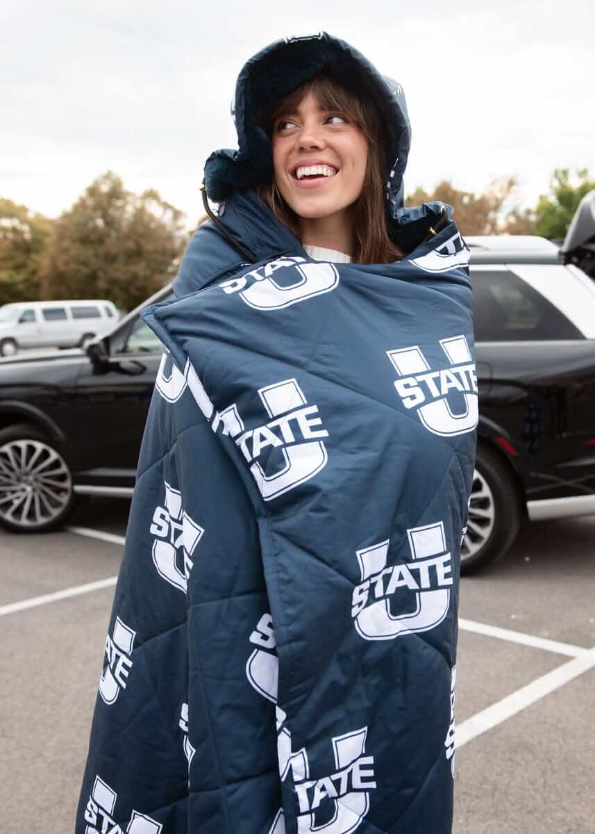 Woman wrapped in navy Utah State Aggies hooded Minky blanket at tailgate.