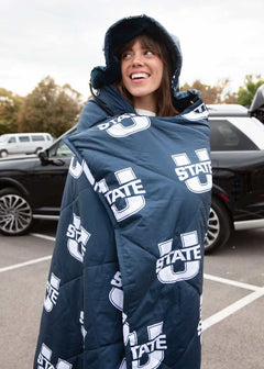 Woman wrapped in navy Utah State Aggies hooded Minky blanket at tailgate.