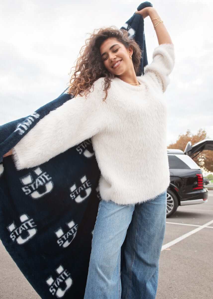 Woman twirling in parking lot with navy Utah State Aggies throw blanket draped over shoulders.