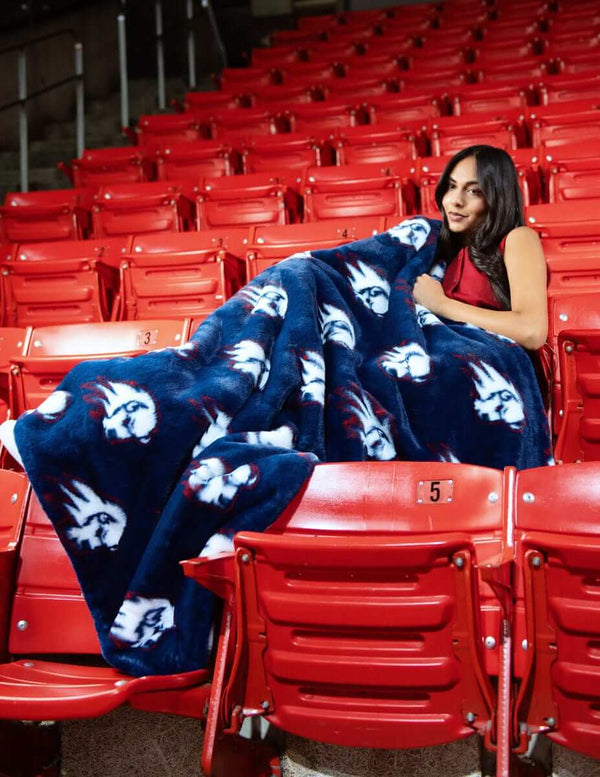 Woman wrapped in navy Utah Tech Trailblazers logo blanket sitting on red stadium seats.