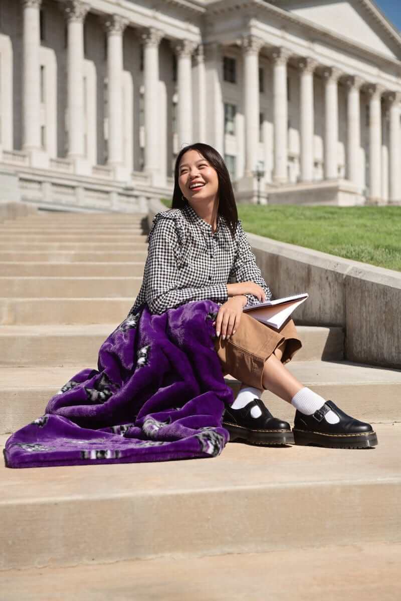 Woman sitting on capitol steps with purple Weber State Wildcats blanket and notebook.