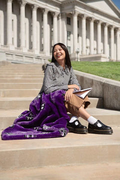 Woman sitting on capitol steps with purple Weber State Wildcats blanket and notebook.