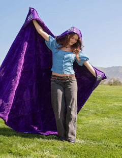 Woman wearing purple Weber State Wildcats hooded blanket outdoors on green lawn.