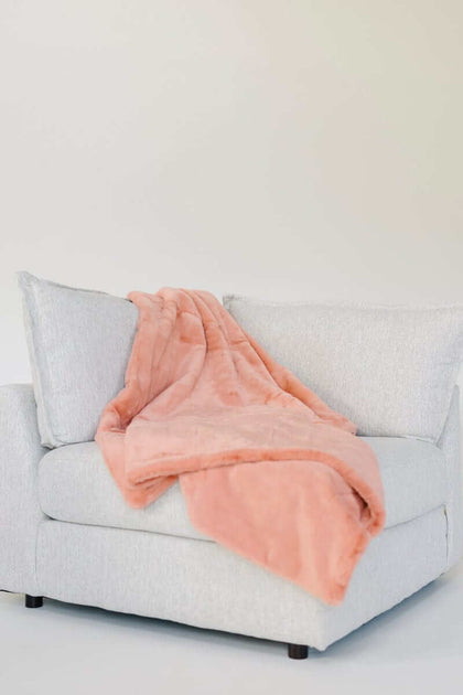 Lush Tawny Spice Blanket draped over a light gray couch, showcasing its coral hue and plush texture.