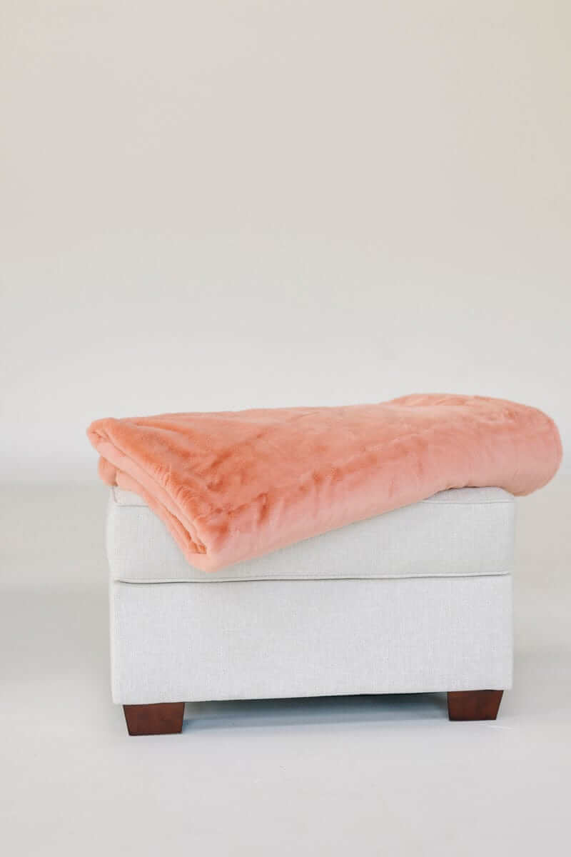 Minky Couture Lush Tawny Spice Blanket draped over a stylish ottoman, showcasing its plush texture and coral hue.
