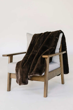 Lush Espresso Blanket draped over a modern wooden chair, showcasing its plush brown texture and cozy appeal.