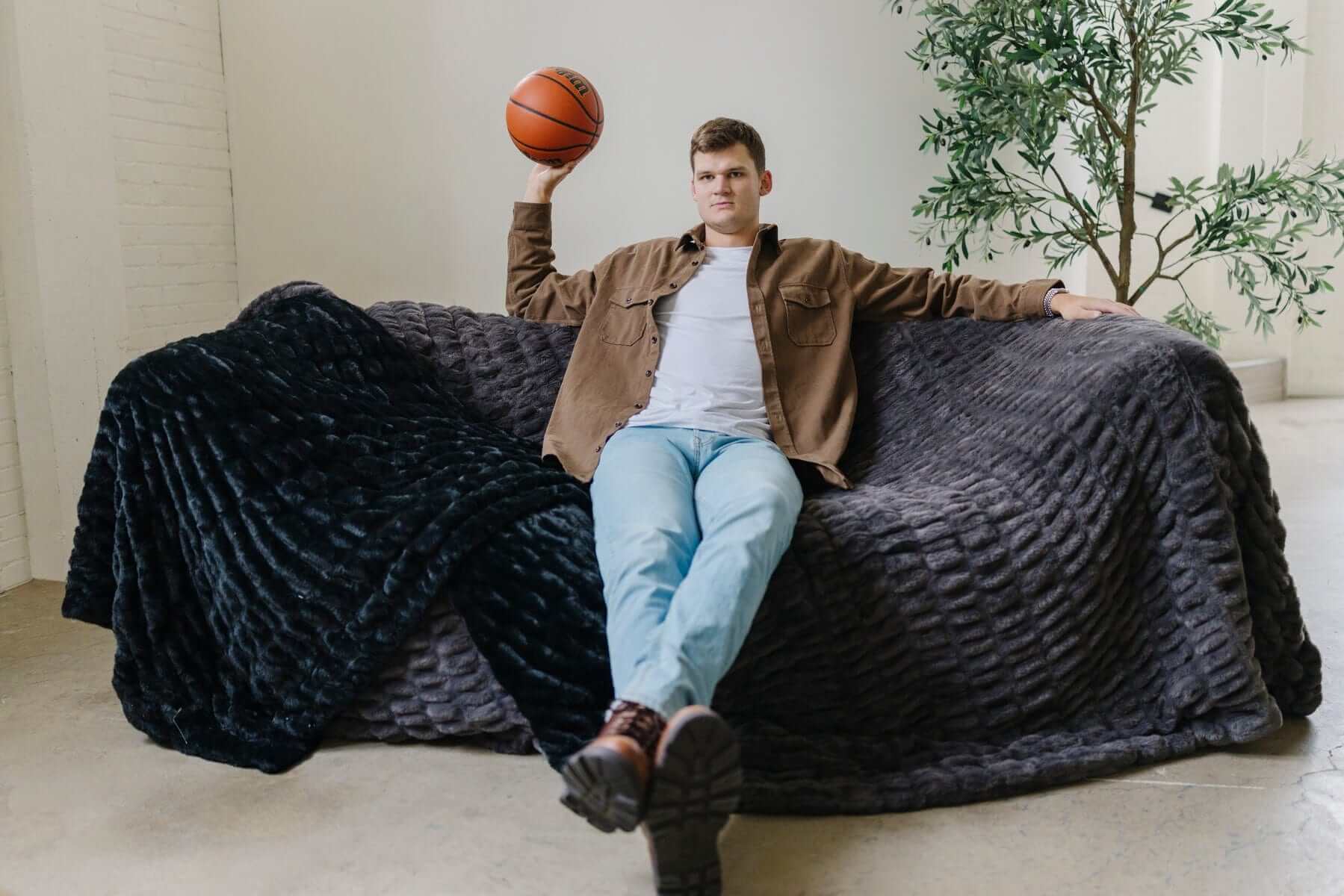 Walker Kessler on a sofa covered in Biggest Hugs Charcoal weighted blanket with a basketball.