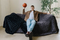 Walker Kessler on a sofa covered in Biggest Hugs Charcoal weighted blanket with a basketball.