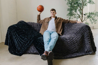 Walker Kessler on a sofa covered in Biggest Hugs Charcoal weighted blanket with a basketball.