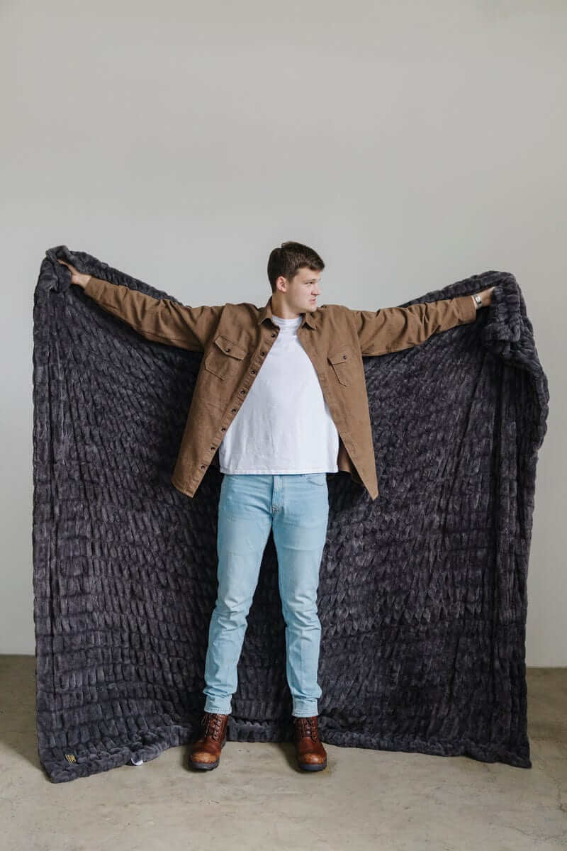 Walker Kessler standing with arms outstretched holding a large charcoal Minky Blanket.