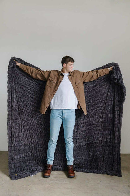 Walker Kessler standing with arms outstretched holding a large charcoal Minky Blanket.
