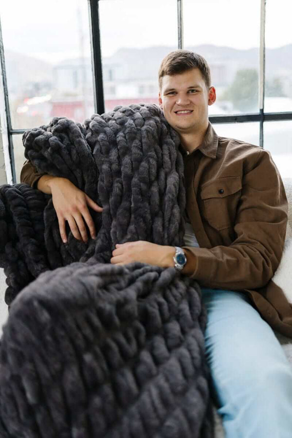Walker Kessler in a chair with a chunky charcoal weighted blanket wrapped around him.