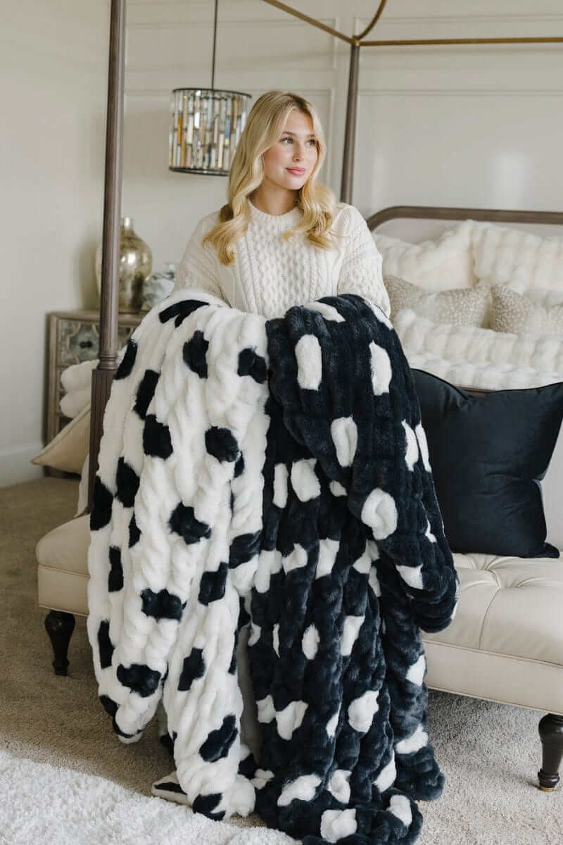 Woman holding large navy and white patterned Minky blankets by a bed.