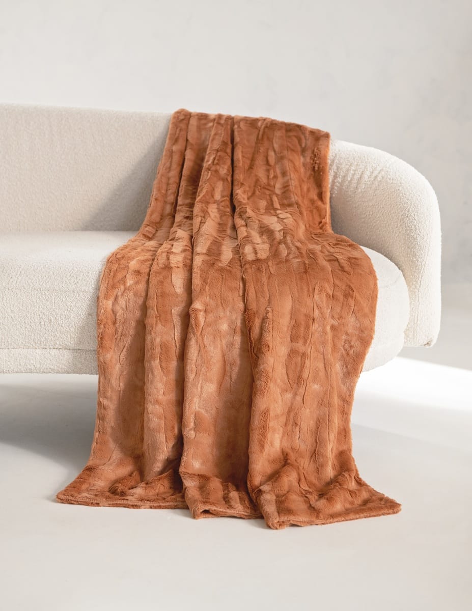 A rust-brown faux fur throw Minky Couture Adobe Sorbet blanket with a textured, wavy pattern draped over a modern white boucle sofa in a minimalist room.