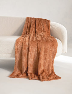 A rust-brown faux fur throw Minky Couture Adobe Sorbet blanket with a textured, wavy pattern draped over a modern white boucle sofa in a minimalist room.
