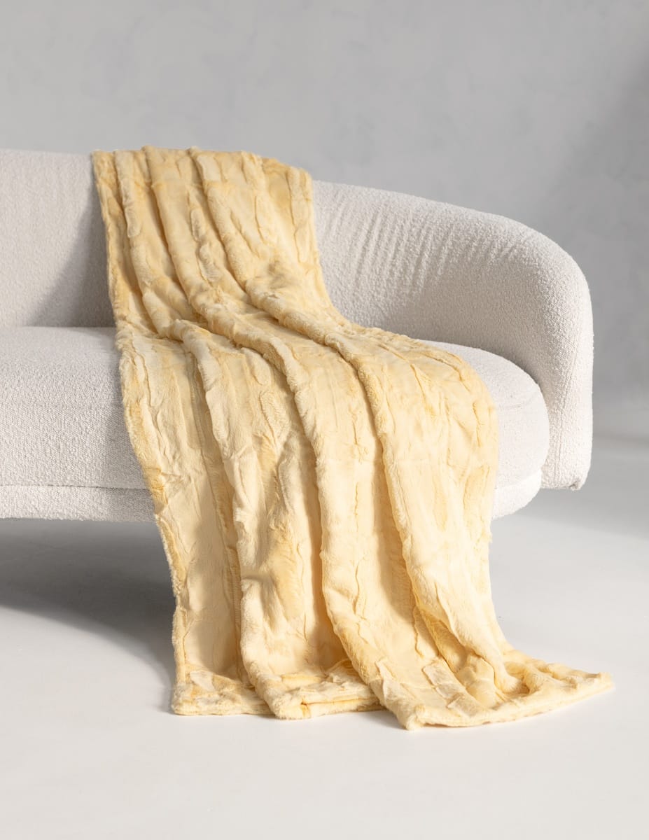 A Sorbet Butter Yellowthrow blanket draped over a modern white curved armchair in a clean studio setting.