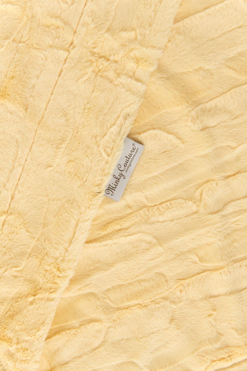 A close-up of Couture Sorbet Butter Yellow blanket with a textured crinkle pattern and a small white brand tag reading 'Minky Couture'.