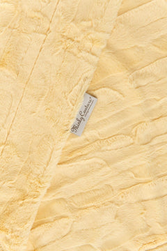 A close-up of Couture Sorbet Butter Yellow blanket with a textured crinkle pattern and a small white brand tag reading 'Minky Couture'.