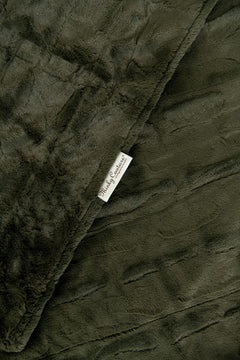 A close-up of a Minky Couture Sorbet Deep Moss  blanket with a textured quilted pattern and a small white brand tag reading 'Mildly Comfortable'.