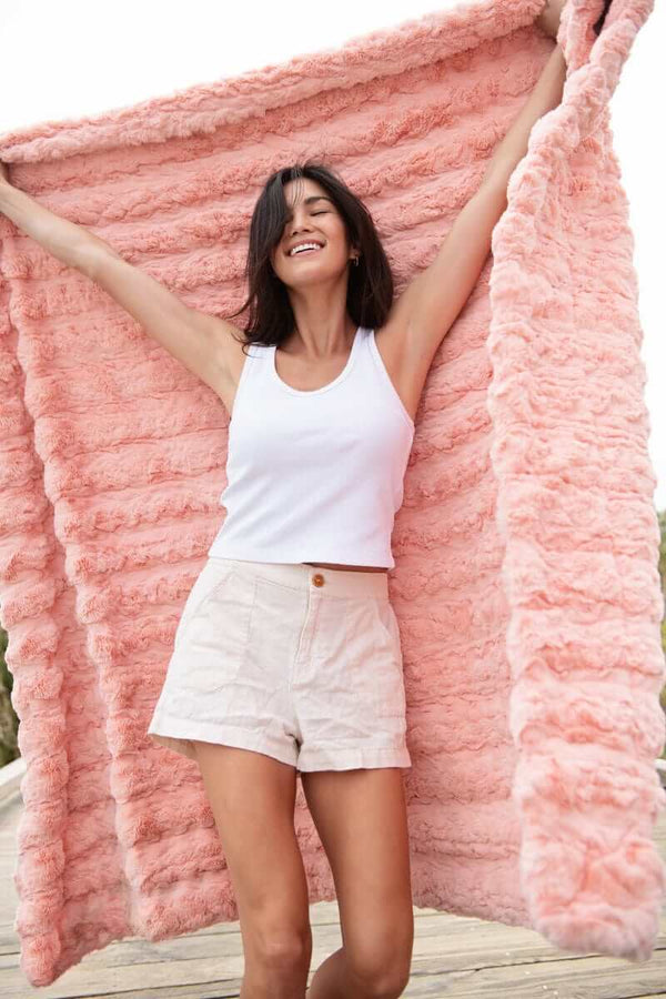 A woman joyfully holding the Ultra Sorbet Spring Blossom Blanket in soft pink, showcasing its plush texture and cozy appeal.