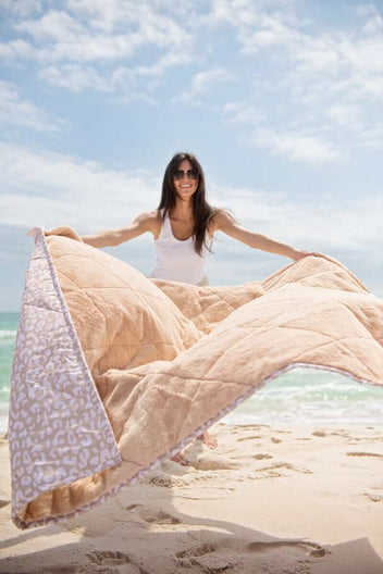 Everywhere Blanket Tan Cheetah being held by a woman on the beach, showcasing the quilted design and prints.