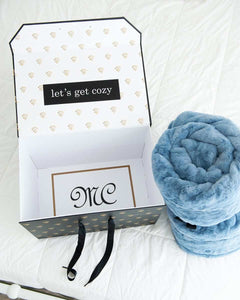Minky Couture gift box with “let’s get cozy” message beside rolled plush blue Minky blanket.
