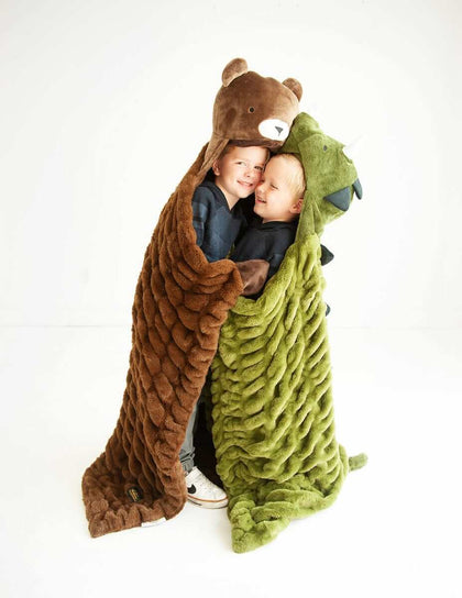 Two children joyfully cuddling in Huggable Dino and bear-themed blankets, showcasing playful comfort.