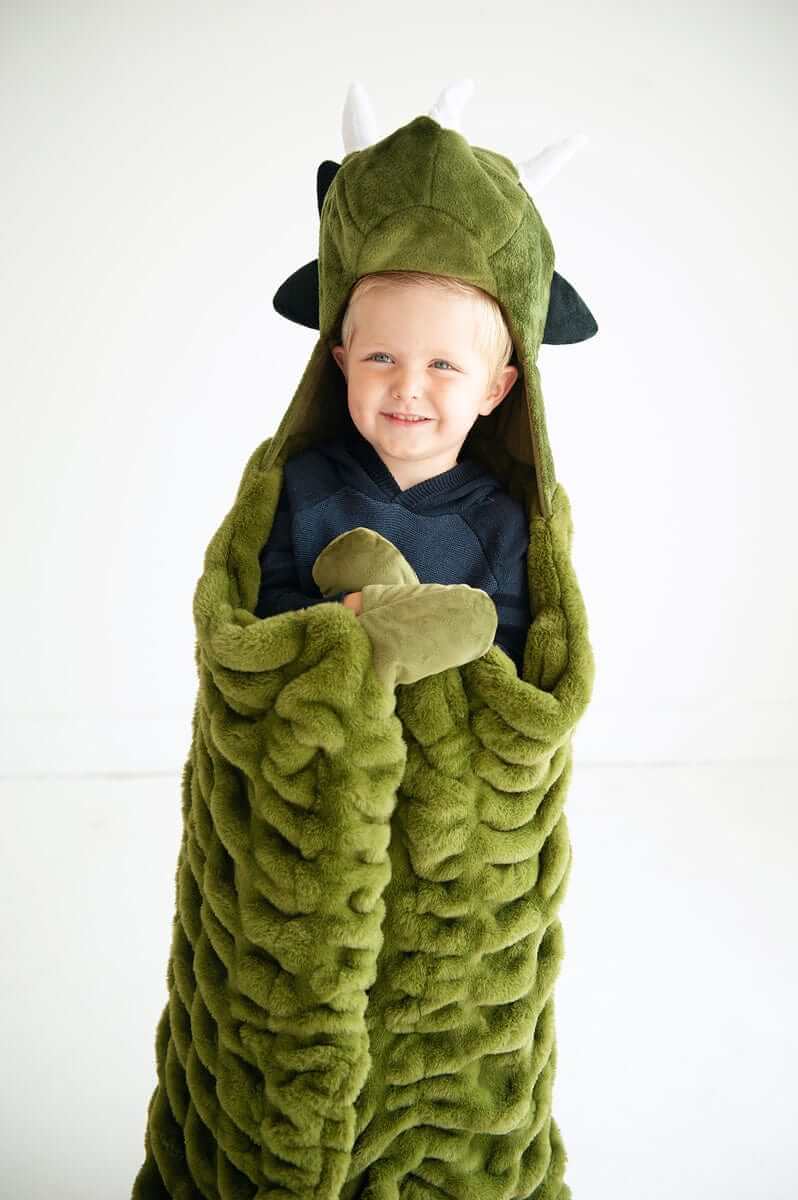 A child wrapped in the Huggable Dino blanket, featuring a triceratops head and cozy green fabric.