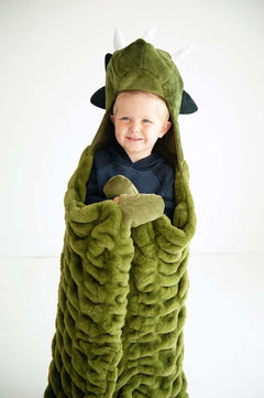 A child wrapped in the Huggable Dino blanket, featuring a triceratops head and cozy green fabric.