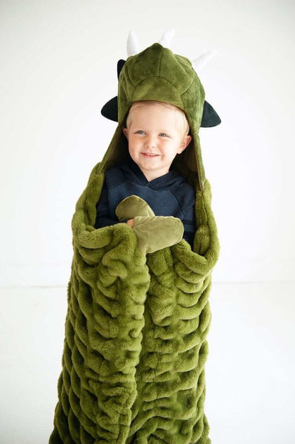 A child wrapped in the Huggable Dino blanket, featuring a triceratops head and cozy green fabric.