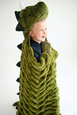 A child laughing while wrapped in the Huggable Dino green blanket with dinosaur head and spikes.