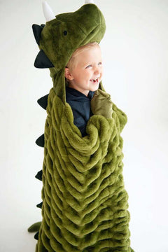 A child laughing while wrapped in the Huggable Dino green blanket with dinosaur head and spikes.