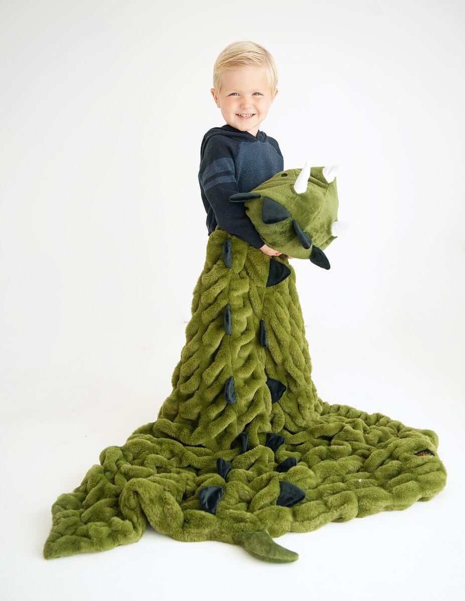Child smiling while wrapped in Huggable Dino blanket with triceratops head, perfect for imaginative adventures.