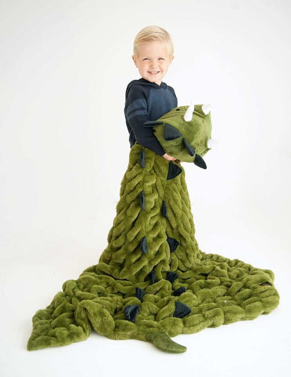 Child smiling while wrapped in Huggable Dino blanket with triceratops head, perfect for imaginative adventures.