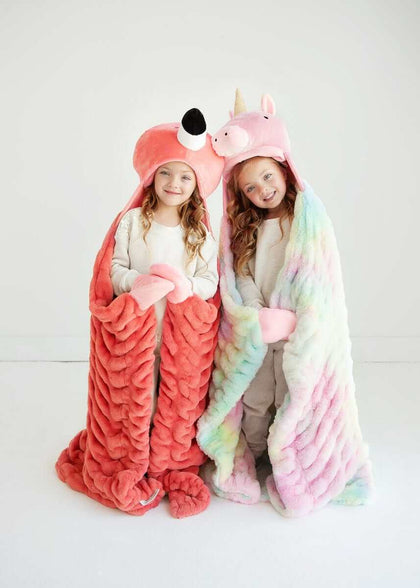 Two girls wearing Huggable Unicorn blankets and animal hats, showcasing comfort and fun for children.