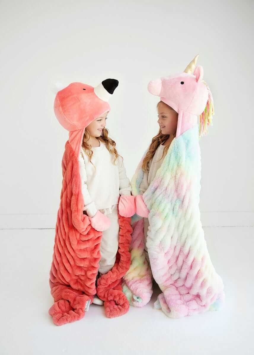 Two children wearing Huggable Unicorn and animal hooded blankets, showcasing colorful designs and cozy comfort.