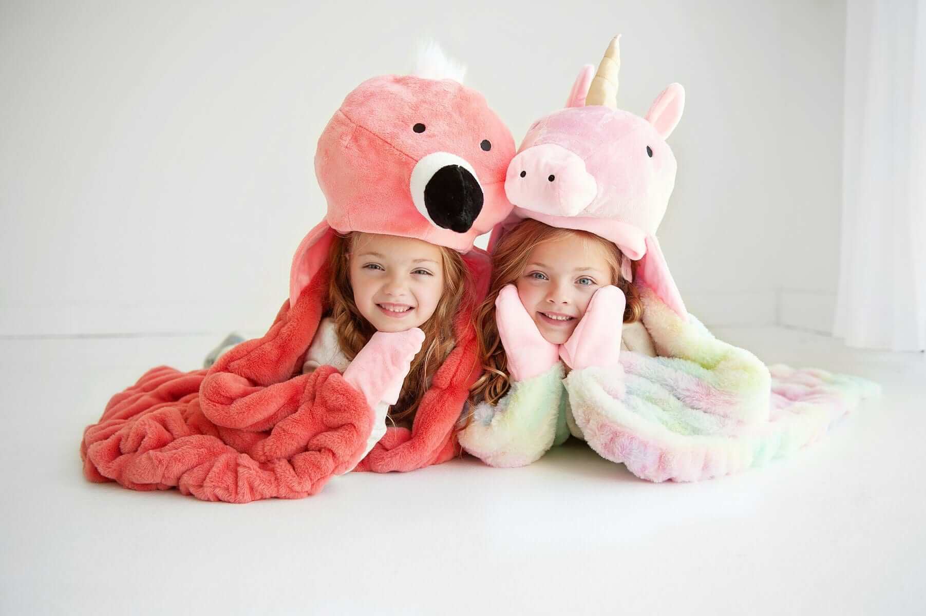 Two children wearing huggable animal hats snuggling in colorful blankets, showcasing the Huggable Unicorn design.